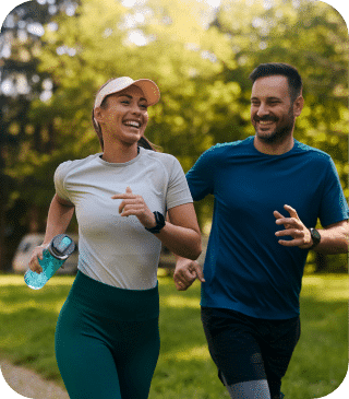 Um homem e uma mulher sorridentes correm lado a lado em um parque, cercados por árvores verdes