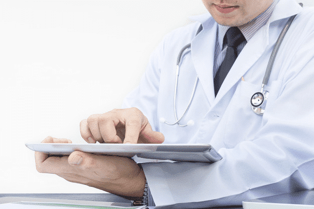 Um médico de jaleco branco e estetoscópio usa um tablet, personificando o futuro da saúde digital