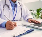 Um médico de jaleco branco escreve em uma prancheta enquanto usa um laptop, representando o atendimento médico na telemedicina
