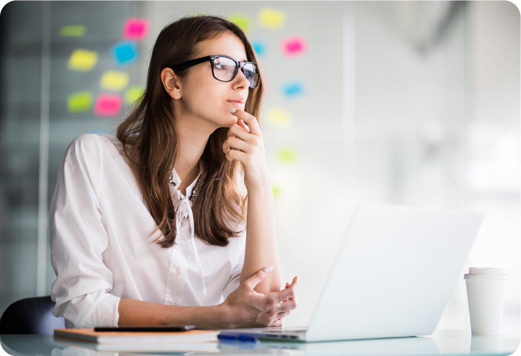 Profissional em ambiente corporativo refletindo sobre estratégias e soluções, representando momentos de planejamento e foco no trabalho. A imagem mostra uma mulher usando óculos, sentada à frente de um notebook, com expressões de concentração e criatividade. Ideal para conteúdos de RH voltados à tomada de decisão, desenvolvimento de talentos, liderança feminina, produtividade e inovação no ambiente de trabalho.
