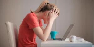Imagem de mulher com a mão na cabeça em frente ao computador