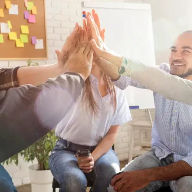 colaboradores de uma empresa estão sentados em uma roda e batendo as mãos em conjunto no alto, para comemorar as aplicações de estratégias de endomarketing de sucesso, o que gera um time produtivo e engajado na empresa