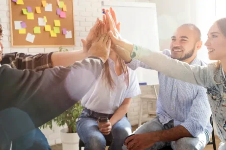 colaboradores de uma empresa estão sentados em uma roda e batendo as mãos em conjunto no alto, para comemorar as aplicações de estratégias de endomarketing de sucesso, o que gera um time produtivo e engajado na empresa